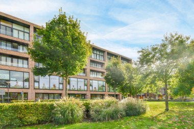 Amsterdam, Hollanda - 10 Nisan 2021: Önünde ağaçlar ve çimenler olan bir apartman dairesi - güneşli bir günde çekilmiş, fakat net değil