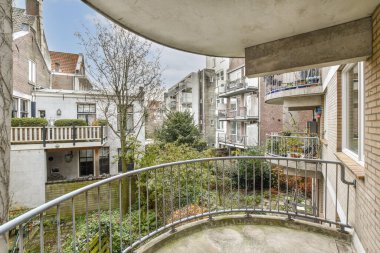 Arka planda ağaçlar ve binalar olan bir dış alan, küçük bir bahçeye bakan bir balkondan alındı.