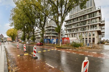 Arka planda binalar ve yere saçılmış yapraklarla dolu boş bir cadde.