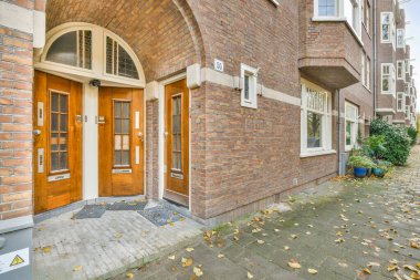 Ortasında kapı olan tuğla bir bina ve yere saçılmış yapraklar ön kapının yanında.