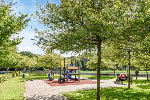 オランダ アムステルダム2021年4月10日 公園内の子供たちの遊び場 青い空の下でベンチに座っている木や人々ストックフォト — ストック写真