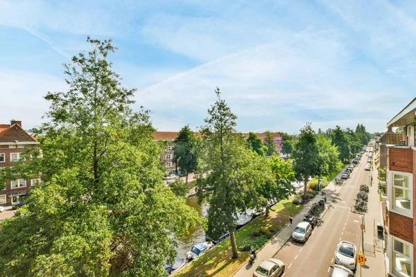 stock image Amsterdam, Netherlands - 10 April, 2021: a city street with cars parked on the side and trees in the fore - eyed view from an apartment window