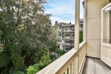Amsterdam, Hollanda - 10 Nisan 2021: arka planda ağaçlar ve binalar olan bir balkon, apartman penceresinden de görüldüğü gibi.
