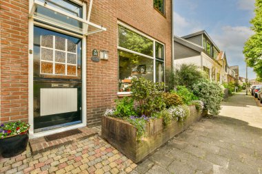 Penceresinde çiçekler olan tuğladan bir ev ve evin girişine giden merdivenlerde saksılar.