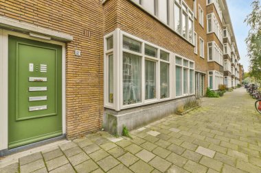 Amsterdam, Hollanda - 10 Nisan 2021: kaldırım boyunca parketmiş bisikletleri olan bir kentsel alanda tuğlalı bir binanın yanındaki yeşil kapı