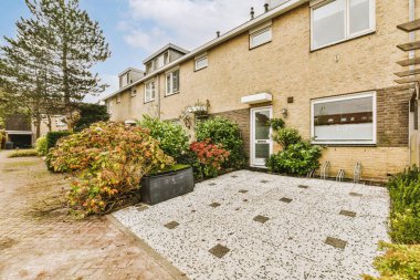 Güneşli bir günde, bahçesinde bitkiler ve çalılar olan bir evin dış görünüşü.