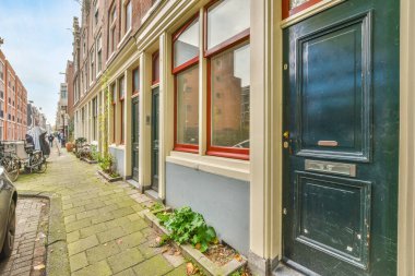 Amsterdam, Hollanda - 10 Nisan 2021: Caddenin her iki tarafında park etmiş arabaların ve binaların olduğu bir şehir caddesi arka planda mavi bir gökyüzü var.