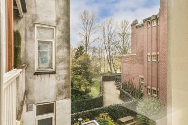 Ön planda ağaçlar ve çalılar olan bir dış alan. Pencereden sokağa bakıyorlar.