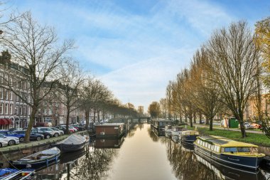 Amsterdam, Hollanda - 10 Nisan 2021: sudaki bazı tekneler ve her iki taraftaki binalar, onlar için de suya yansıyan ağaçlar