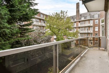 Amsterdam, Hollanda - 10 Nisan 2021: Arka planda ağaçlar ve binalar olan bir dış alan, güneşli bir günde cam korkuluklardan görüldüğü gibi.