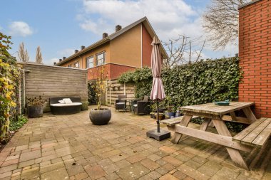 Arka bahçesinde bir piknik masası ve ortasında tuğla duvarlar ve her iki tarafında yeşil bitkiler olan bir bank.