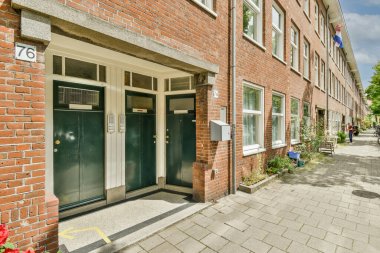 İki tarafında yeşil kapılı tuğla bir bina ve önünde de bir kapı var.