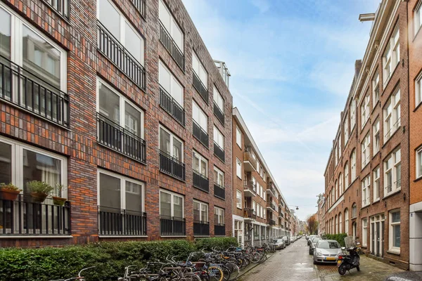 stock image Amsterdam, Netherlands - 10 April, 2021: some bikes parked on the side of a street in an urban area with red brick buildings and green plants growing along the sidewalk