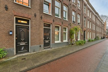 Amsterdam, Hollanda - 10 Nisan 2021: Önünde bisikletleri olan ve kaldırımda yürüyen insanlar olan bir caddenin kenarındaki tuğla bina