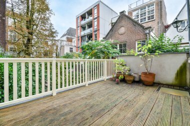 Tepesinde saksı bitkileri olan ahşap bir güverte ve arkasında da bir apartman dairesi.