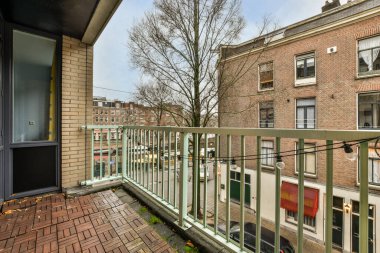 Amsterdam, Hollanda - 10 Nisan 2021: Arka planda ağaçlar ve binalar olan bir balkon, bir apartman penceresinden sokağa bakıyor.
