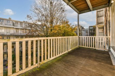 Arka planda ağaçlar ve binalar olan bir balkon, aşağıdaki sokağa bakan bir apartman penceresinden alınmış.