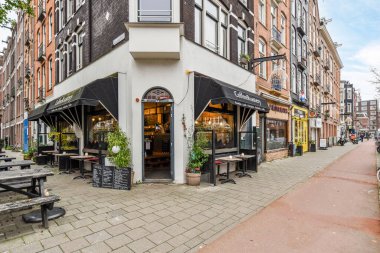 Amsterdam, Hollanda - 10 Nisan 2021: Kafe olarak kullanılan tuğla bir binanın önündeki kaldırım ve masaların bulunduğu bir dış alan