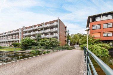 Bir apartmanın önünde köprüye giden yolun her iki tarafında da ağaçlar ve çalılar olan bir köprü.