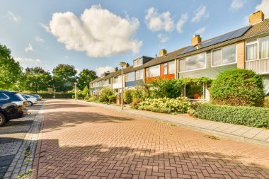 Amsterdam, Hollanda - 10 Nisan 2021: yan tarafında arabalar ve arka tarafında evler olan bir cadde, sağında yeşil çalılıklar var.