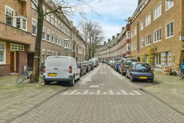 stock image Amsterdam, Netherlands - 10 April, 2021: a city street with cars parked on the curbs and people walking down the street in the distance are bricked buildings