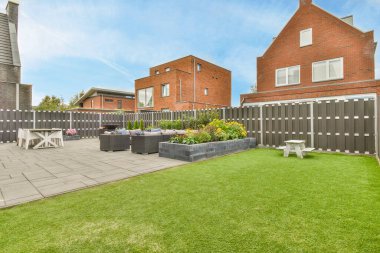 Amsterdam, Hollanda - 10 Nisan 2021: Bahçenin ortasında çimenlik ve teras mobilyaları olan, kırmızı tuğlalı evler ile çevrili bir arka bahçe alanı