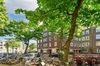 Amsterdam, Hollanda - 10 Nisan 2021: Bazı bisikletler yeşil ağaçlı tuğla apartman binalarının önüne park ettiler