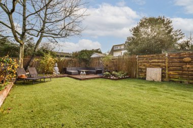 Arka bahçesinde ağaçlar ve çimenler olan bir bahçe, diğer tarafında bir ateş çukuru var.