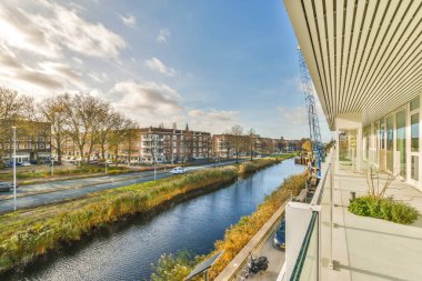Amsterdam, Hollanda - 10 Nisan 2021: Arka planda binalar ve suyun yanında yürüyen insanlar olan bir nehir