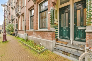 Yeşil kapılı ve pencereli tuğla bir binanın önündeki caddenin kenarına park etmiş bir bisiklet.