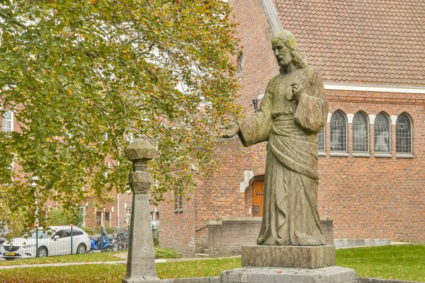 stock image a statue in front of a brick building with a cross on its base and a car parked next to the church