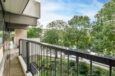 Amsterdam, Hollanda - 10 Nisan 2021: Arkaplanda ağaçlar ve üzerinde mavi gökyüzü olan bir balkon, apartman balkon penceresinden alındı.