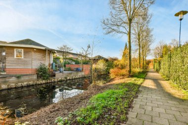 Amsterdam, Hollanda - 10 Nisan 2021: Her iki tarafında su ve ağaçlar olan küçük bir alanın ortasında bir ev var.