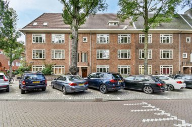 Amsterdam, Hollanda - 10 Nisan 2021: Caddenin her iki tarafında birçok pencere ve kapı olan bir apartmanın önüne park edilmiş bazı arabalar