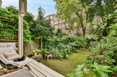 Amsterdam, Hollanda - 10 Nisan 2021: Çevrede bir sürü bitki ve ağaç bulunan bir arka bahçe, birkaç yıldır kullanılan bir şezlong da dahil.