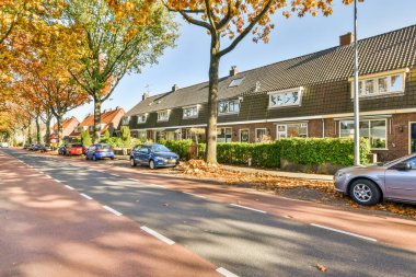 Amsterdam, Hollanda - 10 Nisan 2021: yan tarafında arabalar ve arka tarafında evler olan bir cadde, hepsi birbirine karşı dizilmiş.