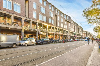 Amsterdam, Hollanda - 10 Nisan 2021: Kenarında arabaları park edilmiş bir şehir caddesi ve sokakta yürüyen insanlar bir apartman dairesi.