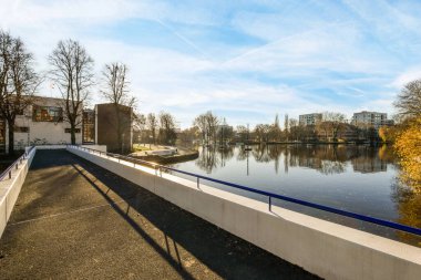 Amsterdam, Hollanda - 10 Nisan 2021: Arka planda ağaçlar ve binalar olan bir nehir, su kenarına bakan bir köprüden alındı