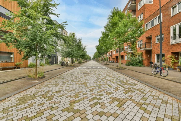 stock image Amsterdam, Netherlands - 10 April, 2021: an empty street in the middle of a city with bricked buildings and green trees on either side of the road