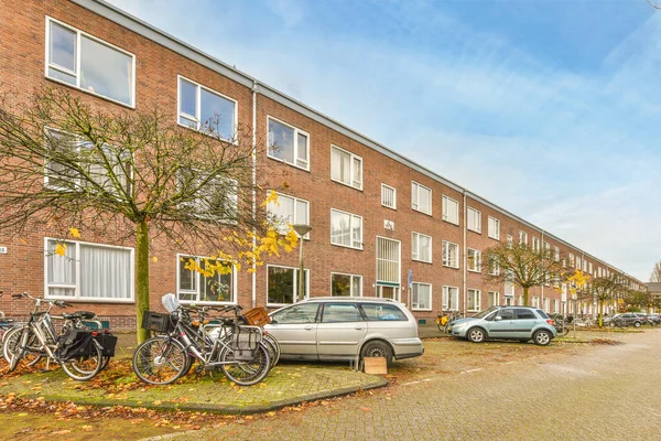 stock image Amsterdam, Netherlands - 10 April, 2021: some bikes parked on the side of a street in front of a brick building with two cars parked next to it