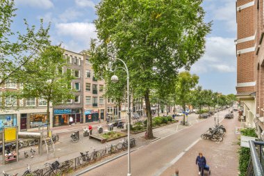 Amsterdam, Hollanda - 10 Nisan 2021: İnsanların yürüdüğü ve bisikletlerin yol kenarına park edildiği bir şehir sokağı