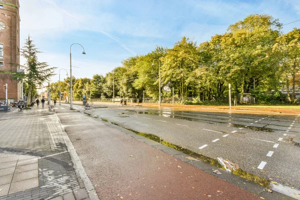 stock image Amsterdam, Netherlands - 10 April, 2021: a city street with people walking on the sidewalks and trees in the background, taken from a low angle