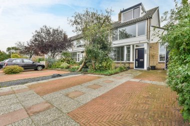 Amsterdam, Hollanda - 10 Nisan 2021: yan tarafında arabalar park edilmiş ve yol boyunca çalılıklar büyüyen bir evin önündeki tuğlalı bir garaj yolu