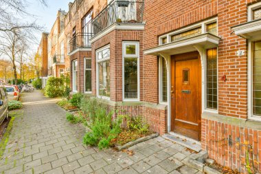 Amsterdam, Netherlands - 10 April, 2021: a brick building on the side of a street with cars parked in front and trees lining the sidewalk behind it