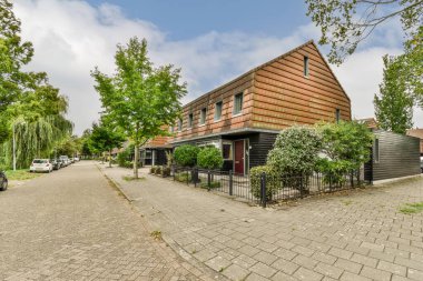 Amsterdam, Hollanda - 10 Nisan 2021: Bir caddenin ortasında, yan tarafında arabalar park edilmiş bir ev ve arkasında ağaçlar var.