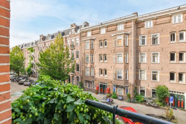 Amsterdam, Hollanda - 10 Nisan 2021: Balkonunda bazı binalar ve yeşil santraller bulunan bir dış alan, kırmızı tuğlalı bir binanın önünde