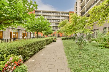Amsterdam, Hollanda - 10 Nisan 2021: Her iki tarafında yeşil çimenler ve ağaçlar olan bir apartman dairesi, oraya giden tuğla bir yol var.