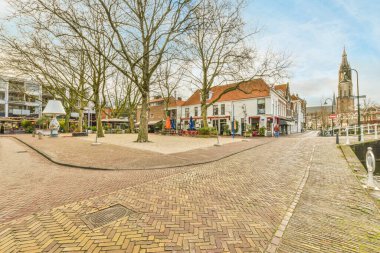 Her iki tarafında ağaçlar ve binalar olan küçük bir kasabanın ortasında boş bir cadde var. Mavi bir gökyüzü var.