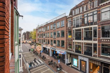 Amsterdam, Hollanda - 10 Nisan 2021: Bir çok binanın bulunduğu bir şehir caddesi ve önünde yürüyen insanlar, bir apartmandan alındı.