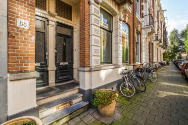 Eski tuğlalı bir binanın önünde, pencereli ve kepenkleri kapalı bir binanın önüne parketmiş bisikletler.